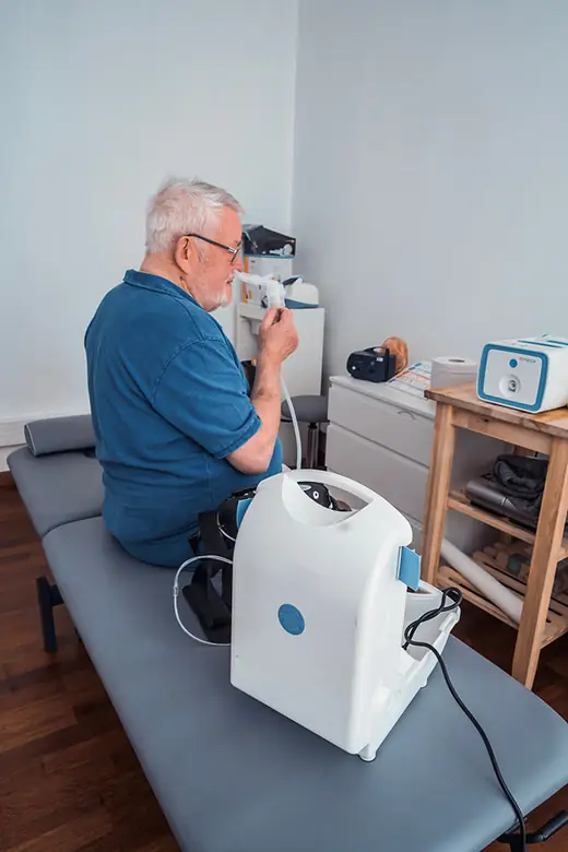 Un patient apprend à bien prendre son aérosol, avec un concentrateur d'oxygène à côté de lui