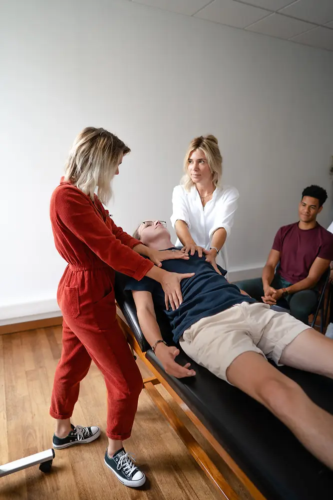 Atelier d'éducation thérapeutique : une kinésithérapeute guide un patient allongé, devant les participants