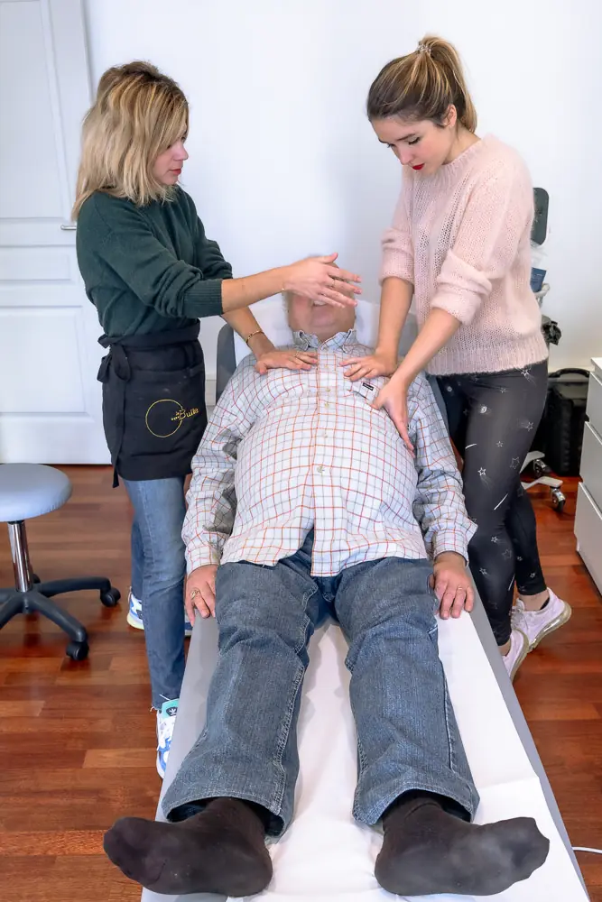Séance de drainage bronchique : deux kinésithérapeutes, les mains sur le thorax du patient allongé